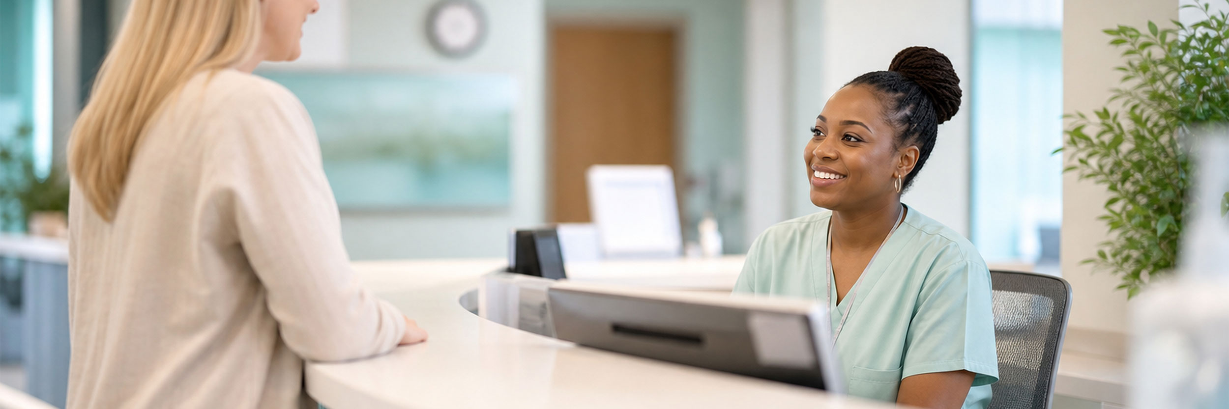 HOA_desktop Healthcare office assistant in scrubs smiling and assisting a patient at the reception desk of a modern medical clinic.