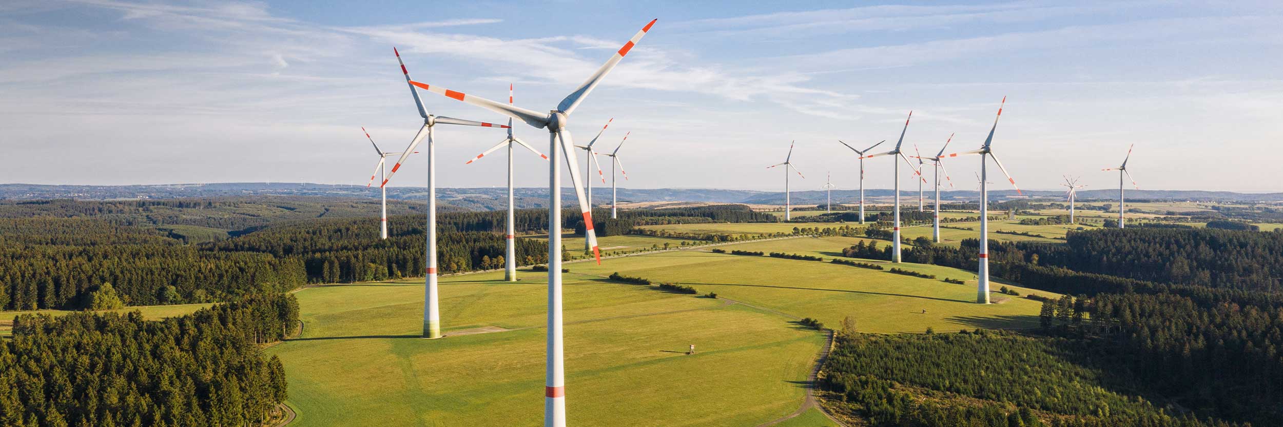 SRE_desktop Aerial view of a wind farm with multiple wind turbines generating renewable energy across green fields and forested landscapes.