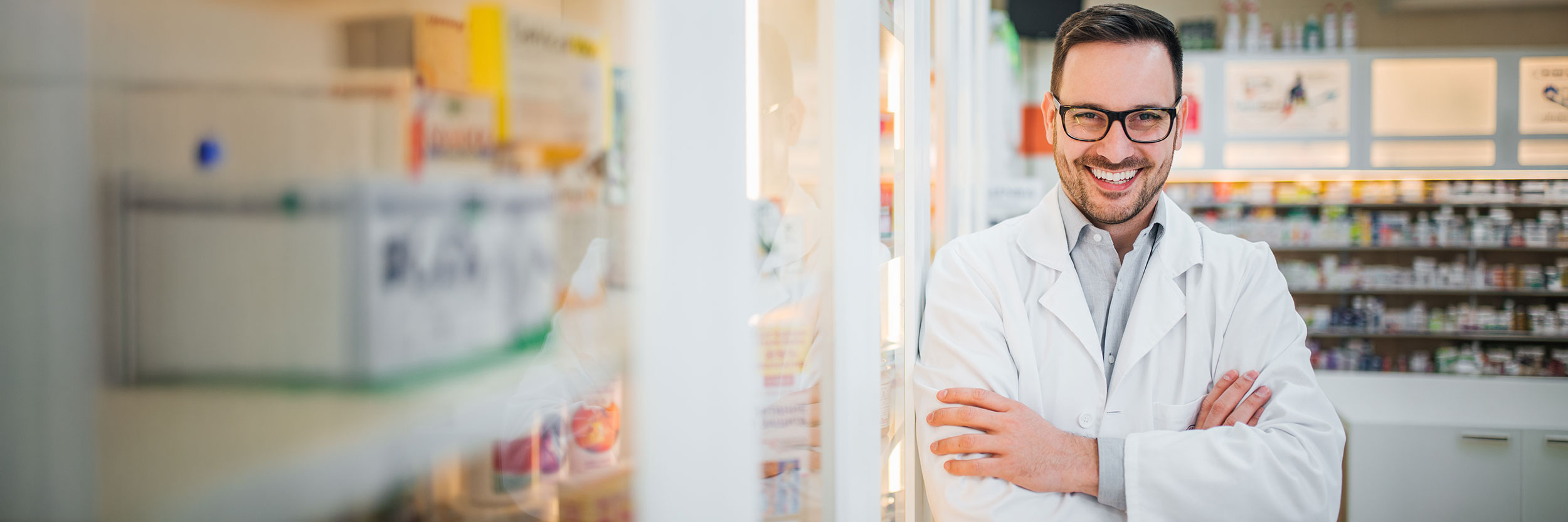 PA_Pr_desktop Smiling male pharmacist standing confidently in a pharmacy, wearing a white lab coat and glasses, Pharmacy Assistant with Practicum