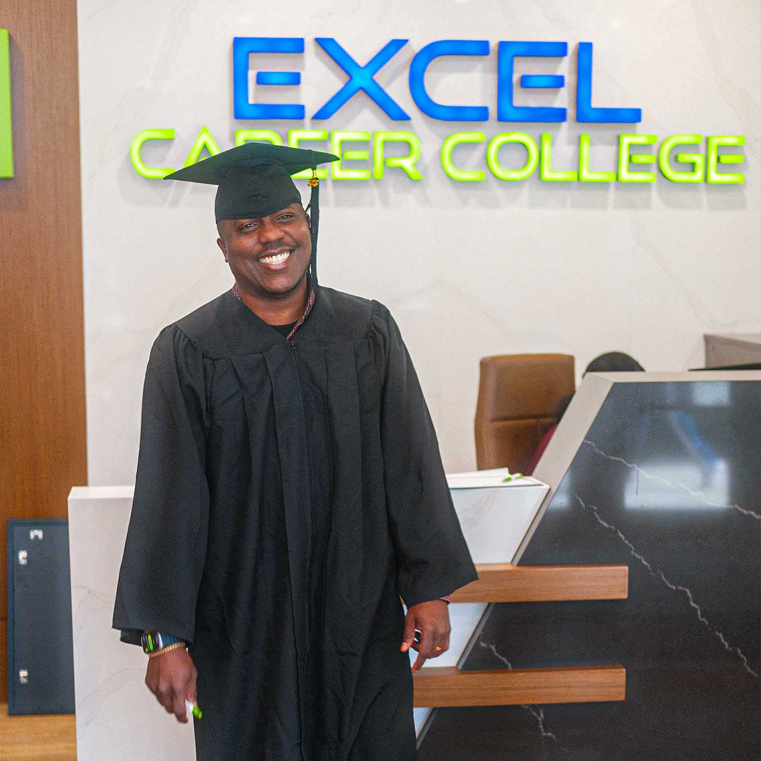 Graduate in cap and gown smiling at Excel Career College reception area